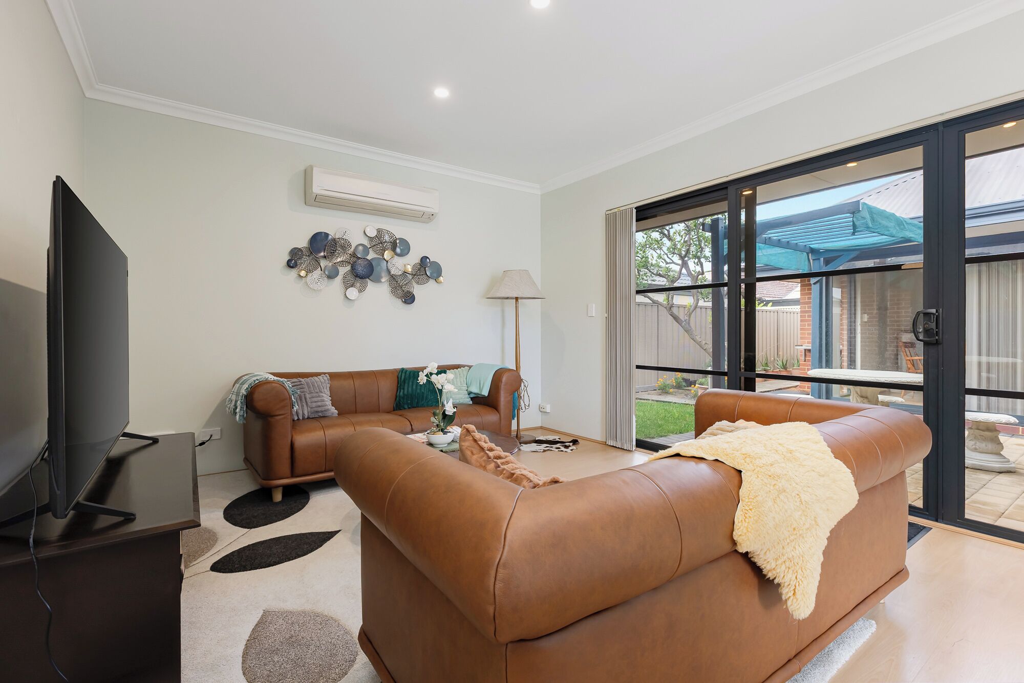 A modern living room with a brown leather sofa, a flat-screen TV, and a decorative wall piece.