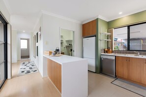 A modern kitchen with a central island, a refrigerator, a dishwasher, and wooden cabinets. - Charming 3 bedroom, 2 bathroom home Tuart Hill home! Perfectly located between Perth CBD and the coast. Sleeps 6 with a king, double & adjustable single beds plus reverse cycle air-con in every bedroom. Ideal for families, couples and longer stays. (Tuart Hill)
