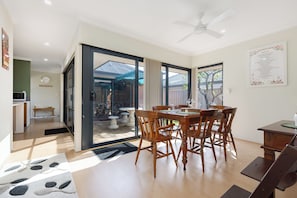 Un coin repas avec une table et des chaises, un ventilateur de plafond et une vue sur une terrasse extérieure, accessible par des portes vitrées.