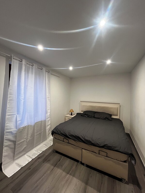 A bedroom with a bed, a nightstand, a lamp, and a curtain.