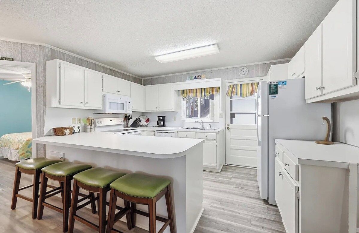 A modern kitchen with white cabinets, a central island with stools, and a refrigerator.