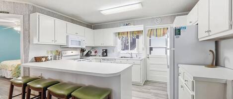 A modern kitchen with white cabinets, a central island with stools, and a refrigerator.