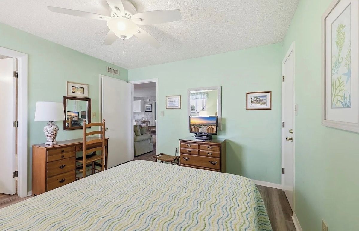 Une chambre à coucher avec un lit, une commode, une chaise et un ventilateur de plafond.