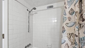 A bathroom with white tiled walls, a bathtub, a showerhead, and a curtain with a shell pattern. - 4/2 bottom floor 1 block from beach (North Myrtle Beach)