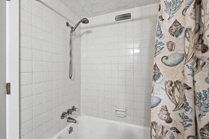 A bathroom with white tiled walls, a bathtub, a showerhead, and a curtain with a shell pattern. - 4/2 bottom floor 1 block from beach (North Myrtle Beach)
