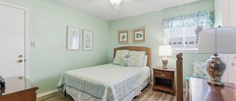 A bedroom with a bed, a nightstand, a lamp, a vase, and a window with blinds.
