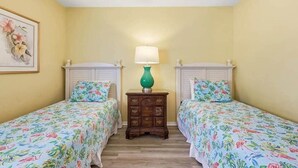 A room with two single beds, a nightstand with a lamp, and a framed floral artwork on the wall. - 4/2 bottom floor 1 block from beach (North Myrtle Beach)