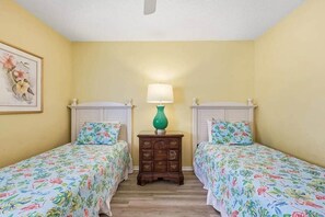 A room with two single beds, a nightstand with a lamp, and a framed floral artwork on the wall. - 4/2 bottom floor 1 block from beach (North Myrtle Beach)