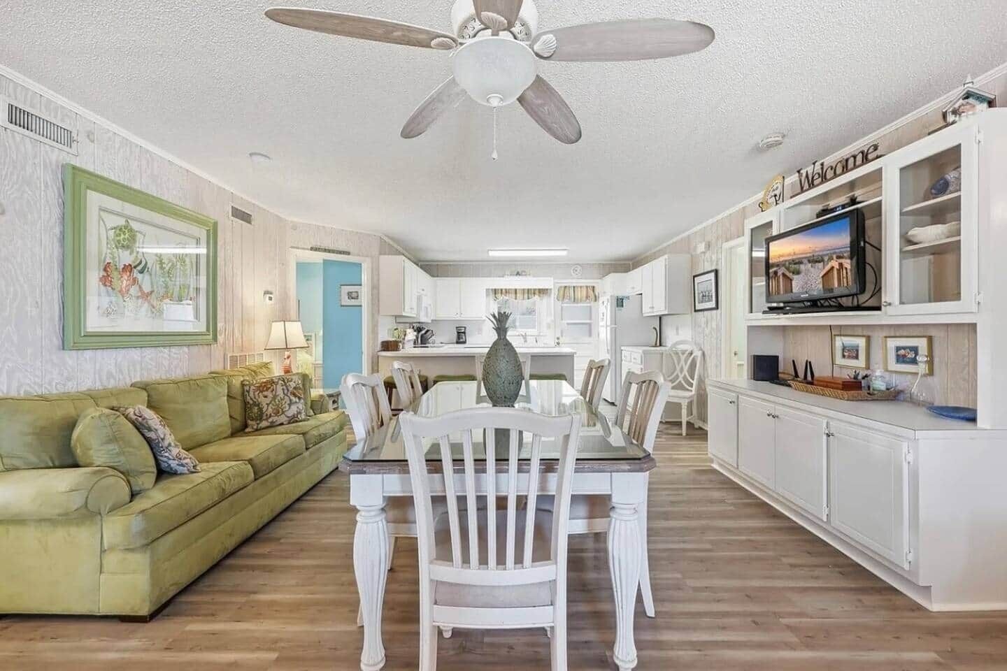 A spacious living area with a dining table, a green sofa, and a ceiling fan.