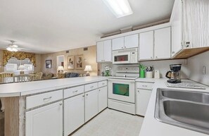 A kitchen with white cabinets, a microwave, an oven, a sink, and a dining area with chairs. - 8BR Beach House | Sleeps 20+ | Walk to Beach (North Myrtle Beach)
