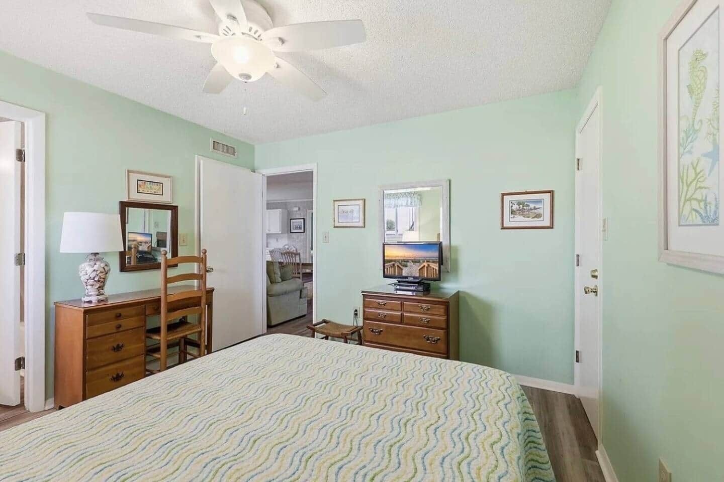 A bedroom with a bed, dresser, mirror, and television.