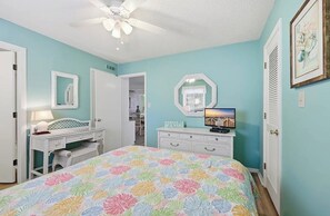 Een slaapkamer met een bed, een kaptafel, een dressoir en een plafondventilator.