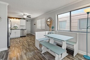 A kitchen with white cabinets, a wooden floor, and a dining area with a bench and table. - Beachfront Escape with Sunset and Marsh Views 14F (North Myrtle Beach)