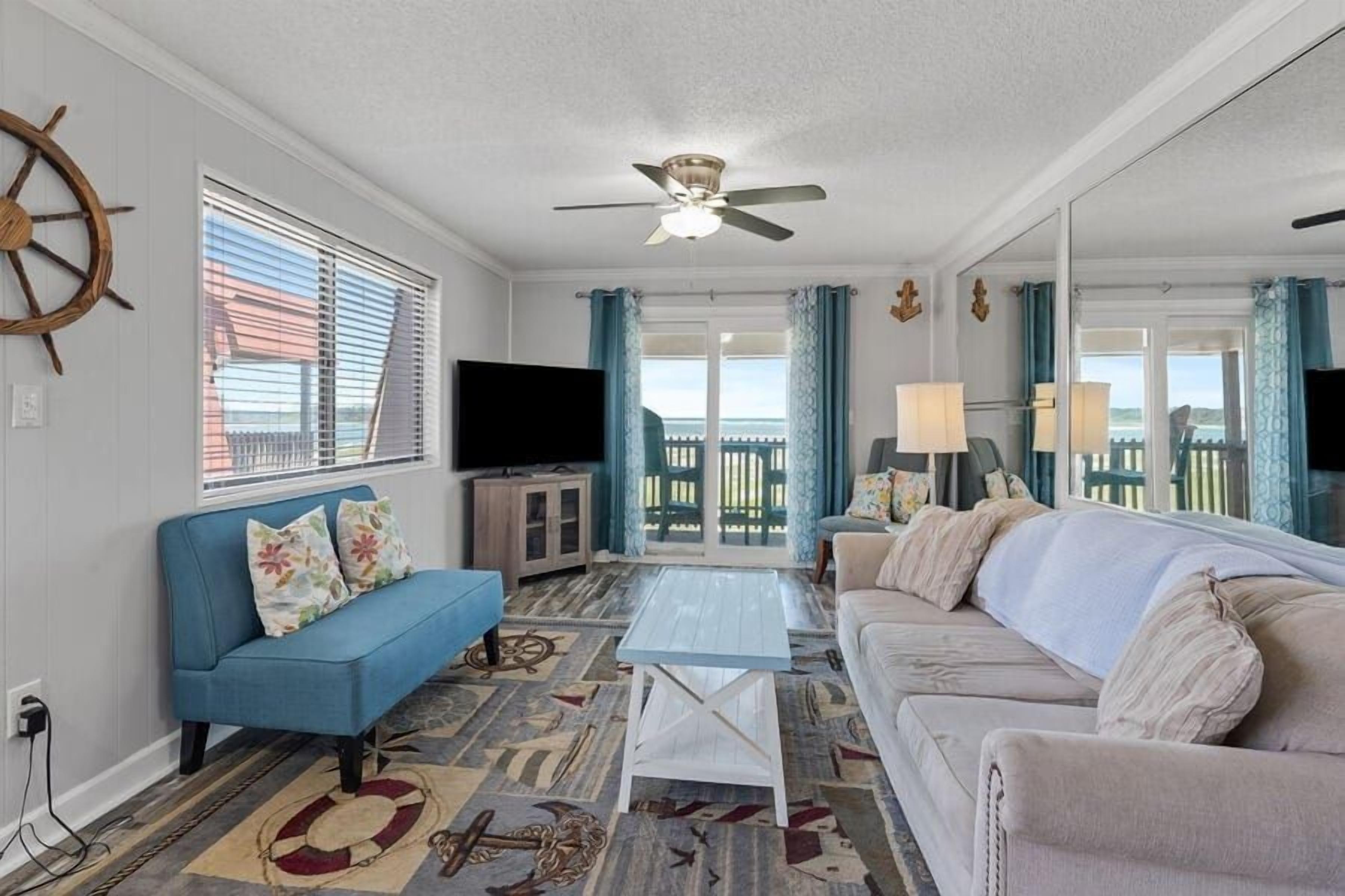 A living room with a blue sofa, a beige sofa, a coffee table, a television, and a ceiling fan.