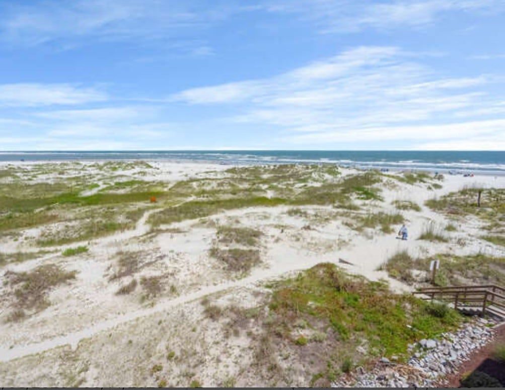 A beach with a wooden walkway leading to the water, sandy dunes, and a clear sky.