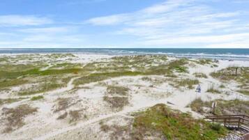 A beach with a wooden walkway leading to the water, sandy dunes, and a clear sky.