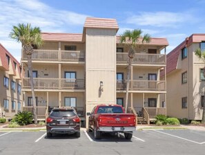 A multi-story hotel with balconies, parking spaces, and palm trees. - Beachfront Escape with Sunset and Marsh Views 14F (North Myrtle Beach)
