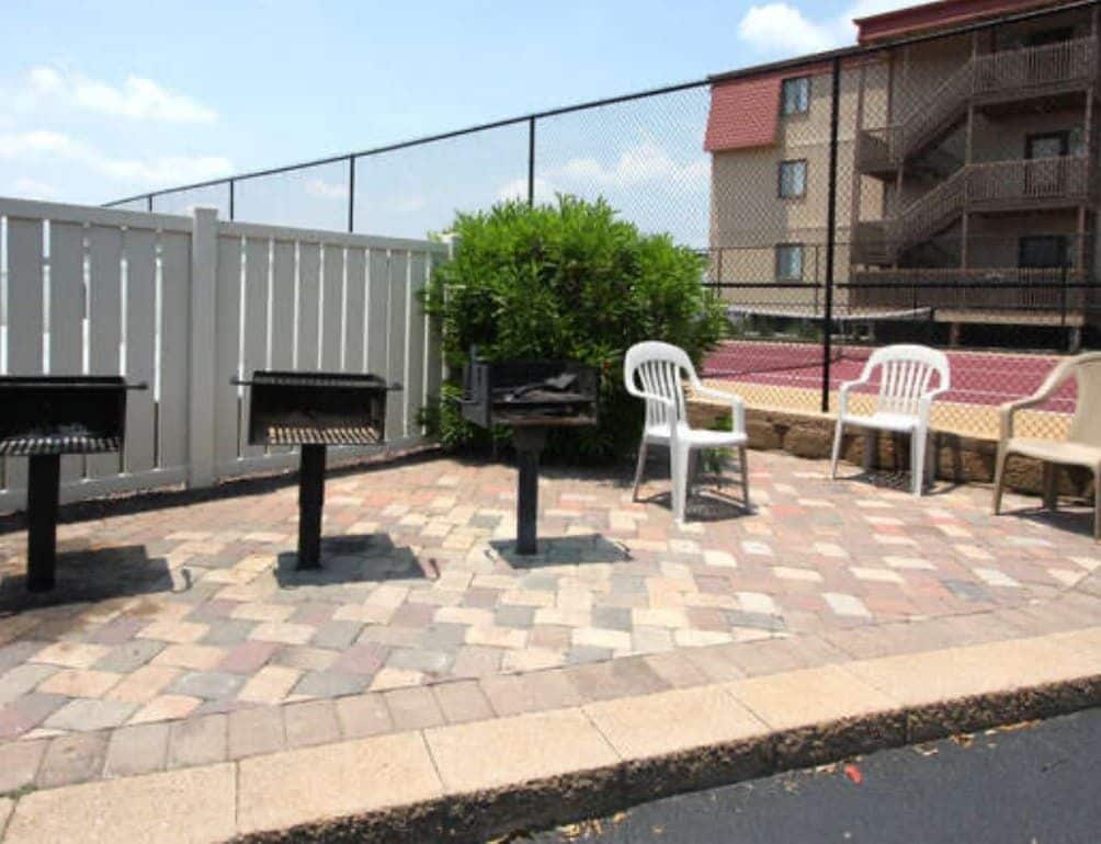 Un patio exterior con una parrilla, sillas y una valla.