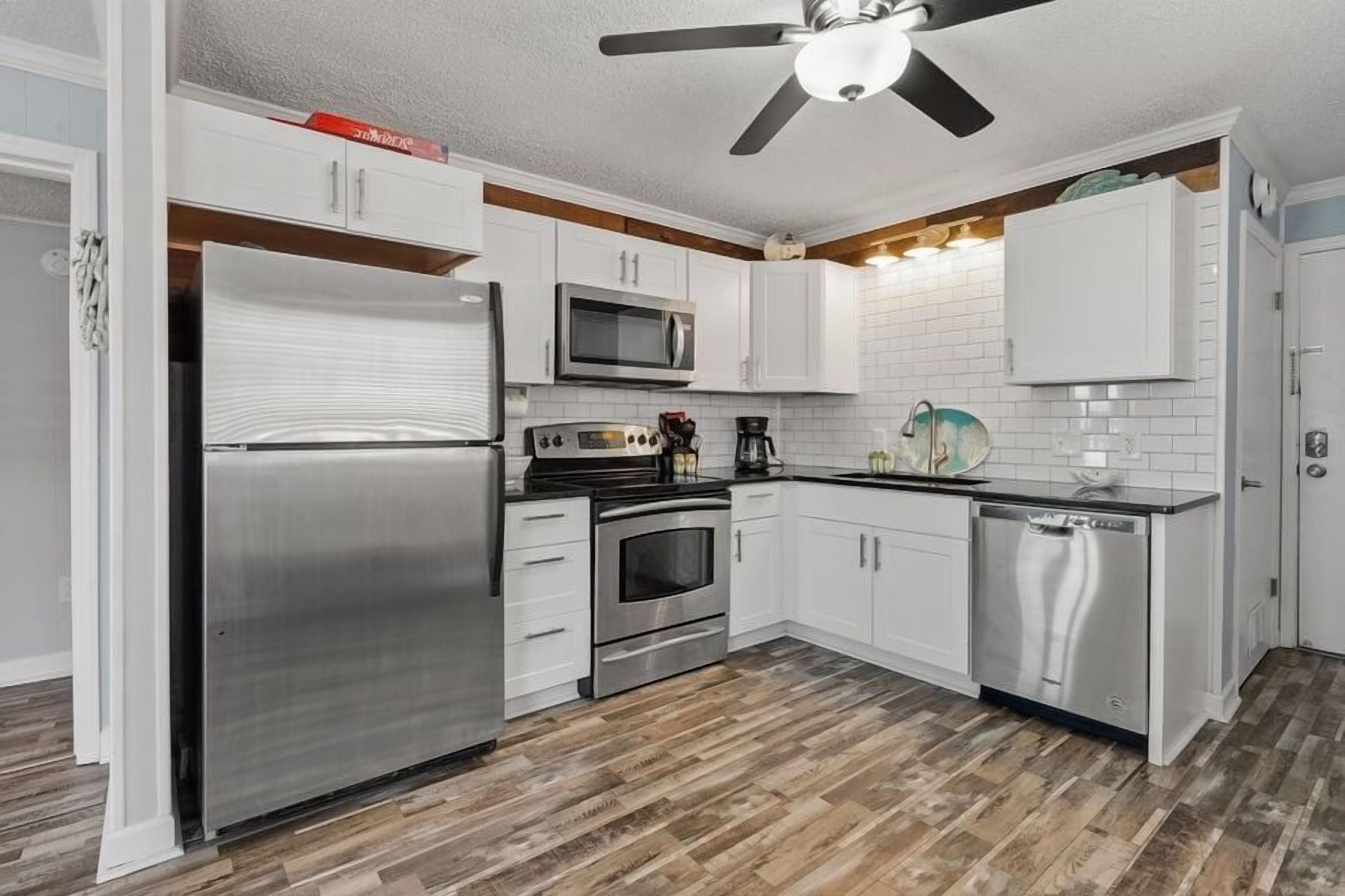 A modern kitchen with white cabinets, stainless steel appliances, and a wooden floor.