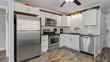 A modern kitchen with white cabinets, stainless steel appliances, and a wooden floor.