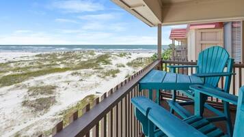 A balcony with a view of the beach, featuring a wooden railing and two blue chairs.