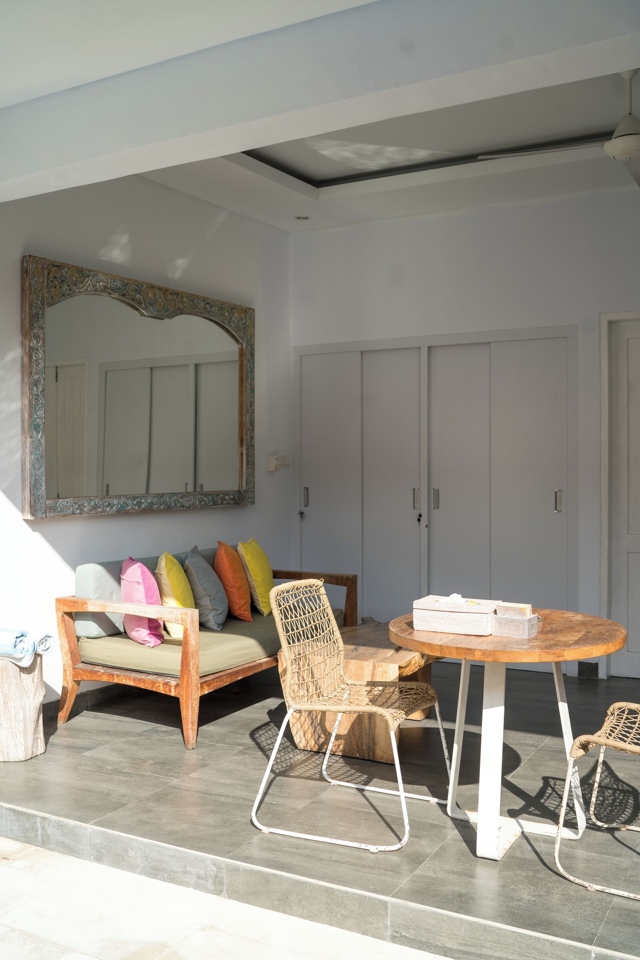 Une pièce comprenant un canapé, un fauteuil en osier, une table ronde et un grand miroir.