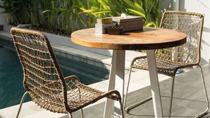 A round wooden table with two wicker chairs, a small potted plant, and a decorative item on the table. - Cozy and Private 1BR Casa Ku Villa in Seminyak (Badung)