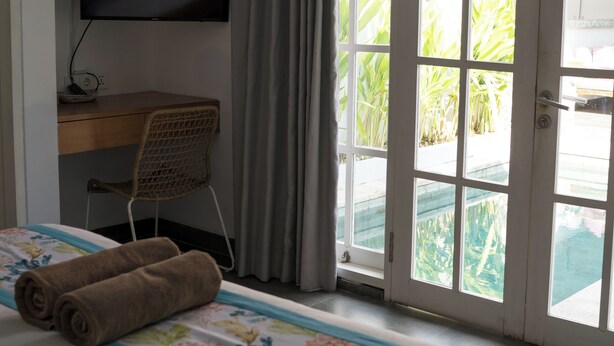 A hotel room with a bed, a desk with a flat-screen TV, a chair, and a window with curtains. - Cozy and Private 1BR Casa Ku Villa in Seminyak (Badung)