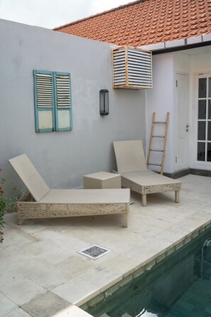A poolside area with two wicker lounge chairs, a ladder, and a door. - Cozy and Private 1BR Casa Ku Villa in Seminyak (Badung)