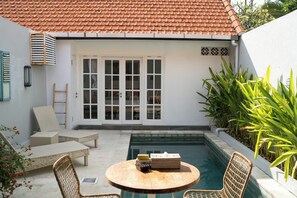 A patio with a pool, wicker furniture, and a white building with a tiled roof. - Cozy and Private 1BR Casa Ku Villa in Seminyak (Badung)