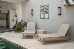 A poolside area with two lounge chairs, a potted plant, and a kitchen in the background. - Cozy and Private 1BR Casa Ku Villa in Seminyak (Badung)