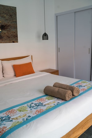 A neatly made bed with a floral bedspread and two rolled towels, a wooden headboard, a nightstand, a wall-mounted lamp, and a wardrobe. - Cozy and Private 1BR Casa Ku Villa in Seminyak (Badung)