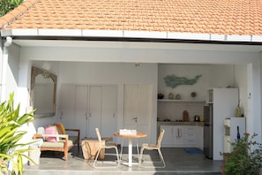A covered outdoor area with a dining set, chairs, a table, and a kitchen area with cabinets and appliances. - Cozy and Private 1BR Casa Ku Villa in Seminyak (Badung)