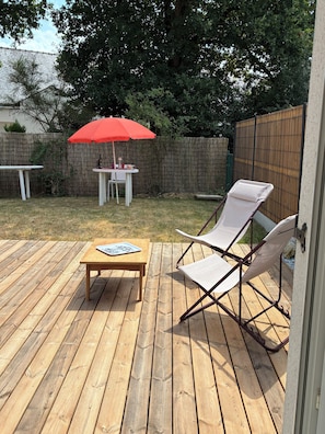 A wooden deck with a table and two chairs, a red umbrella, and a wooden fence in the background. - Maison Marilou, in the heart of the Gulf of Morbihan in Brittany, with friends or family (Plescop)