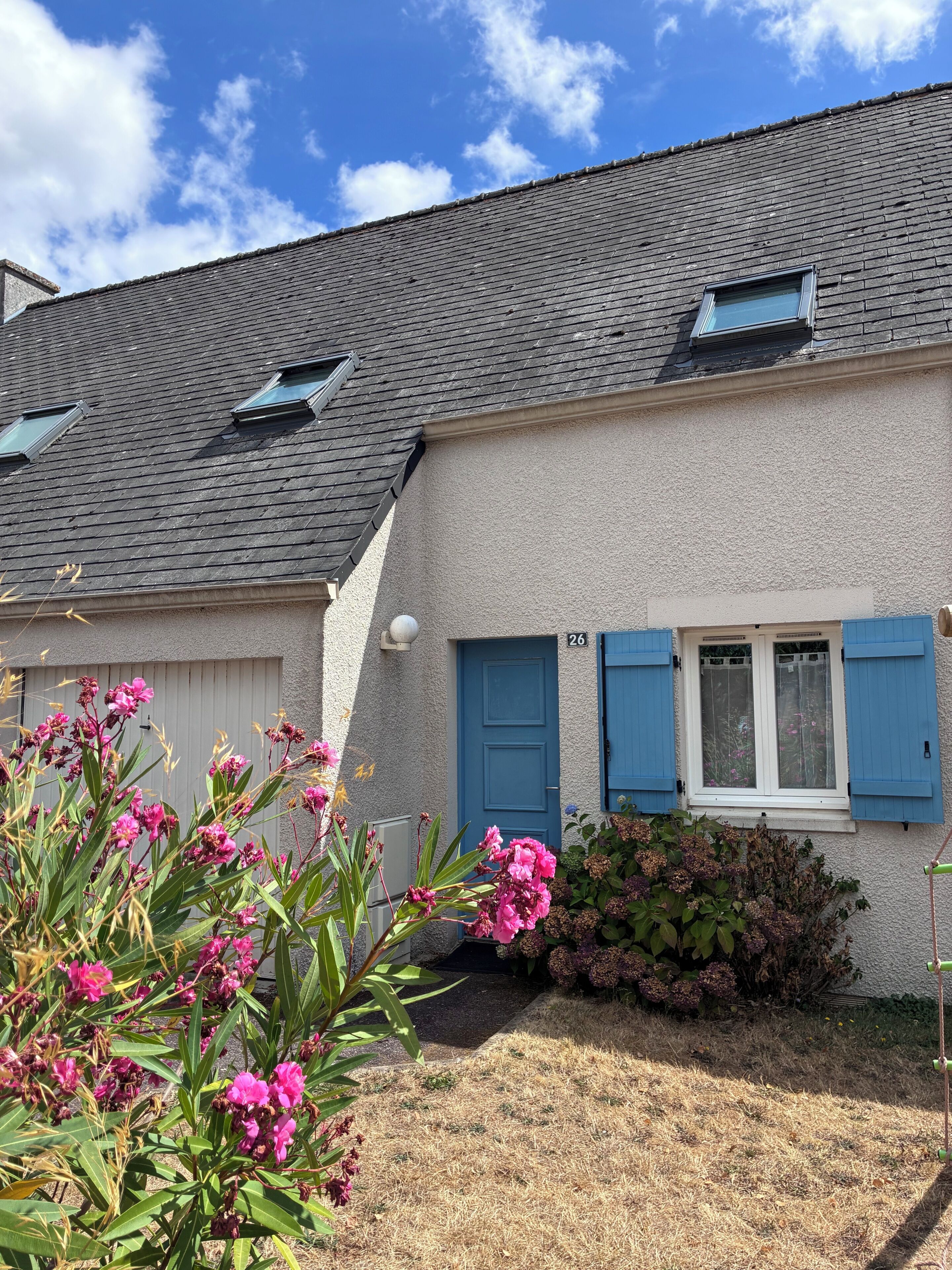 Ein Haus mit grau gefliestem Dach, einer blauen Tür und der Hausnummer 26 an der Wand.