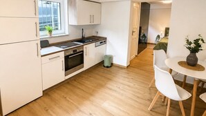 A modern kitchen with white cabinets, a dining area with a round table and chairs, and a view of a bedroom through an open door. - Modern Apartment • 200 m to the lake • Parking Lot Wi-Fi (Möhnesee)