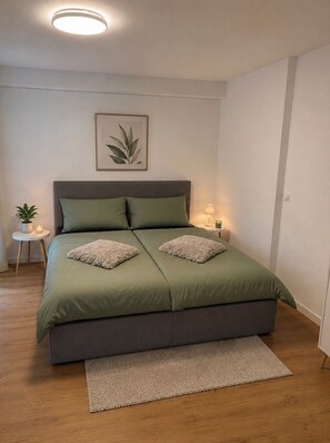 Ein Schlafzimmer mit einem Bett, einem Nachttisch, einer Lampe, einer gerahmten Pflanze und einem Teppich.