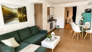 A modern living room with a green sofa, a white coffee table, and a dining area with white chairs. - Modern Apartment • 200 m to the lake • Parking Lot Wi-Fi (Möhnesee)