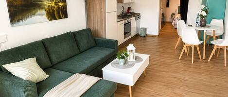 A modern living room with a green sofa, a white coffee table, and a dining area with white chairs.