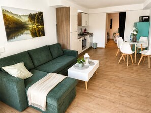 Ein modernes Wohnzimmer mit einem grünen Sofa, einem weißen Couchtisch und einem Essbereich mit weißen Stühlen.