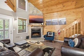 A cozy living room with a fireplace, a mounted TV, and a staircase leading to an upper level. - Bear Run Getaway 3 Bedroom Cabin (Gatlinburg)