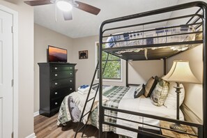 Ein Stockbett mit einer Leiter, eine Kommode, ein Fernseher und ein Fenster mit Jalousien.