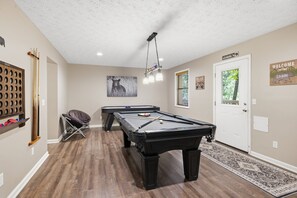 A pool table in a room with a wooden floor, a door with a welcome sign, and a wall with a bear picture. - Bear Run Getaway 3 Bedroom Cabin (Gatlinburg)
