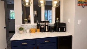 A modern kitchen with a marble countertop, dark blue cabinets, and three pendant lights. - Spacious Family Retreat with Several Living Areas, Backyard with Patio & Pool (Dayton)