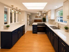 A modern kitchen with dark cabinetry, a central island, and pendant lighting. - Spacious Family Retreat with Several Living Areas, Backyard with Patio & Pool (Dayton)