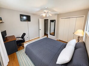 Ein Schlafzimmer mit einem Bett, einem Schreibtisch mit Stuhl, einem Fernseher, einem Deckenventilator und einem Kleiderschrank.