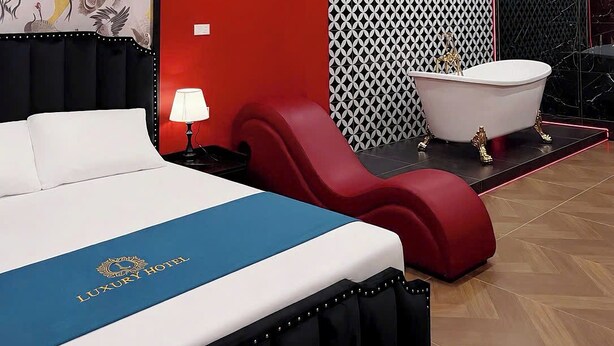 A luxury hotel room with a bed, a red chair, a bathtub, and a wall with a geometric pattern.