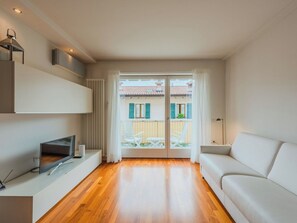 Un soggiorno moderno con una TV a schermo piatto, un divano e un'area pranzo visibile tramite una porta in vetro.