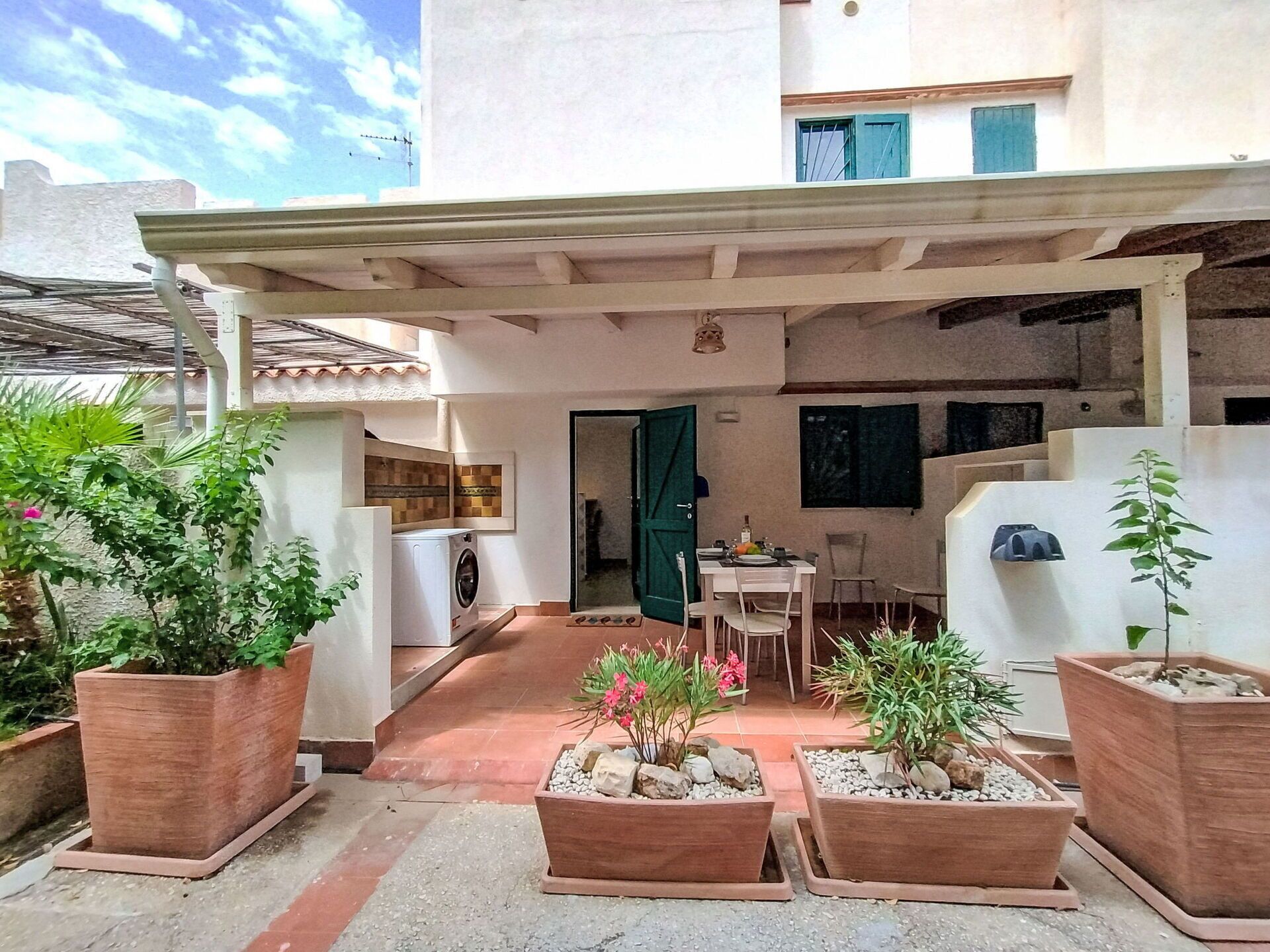 A courtyard with a covered seating area, a washing machine, and potted plants.