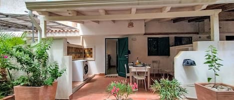 A courtyard with a covered seating area, a washing machine, and potted plants.